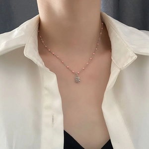 Collier de perles roses avec pendentif Fu argenté porté sur une chemise blanche
