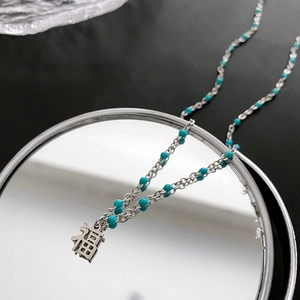 Collier argenté avec perles turquoise et pendentif 'Fu' ajouré sur fond miroir
