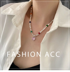 Détail d'un collier de perles colorées avec pendentif cœur rose sur chemise blanche