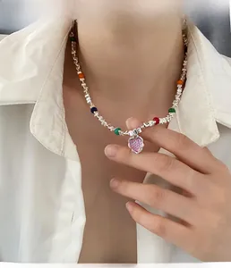 Gros plan du pendentif cœur rose sur une chaîne à perles argentée portée par un modèle