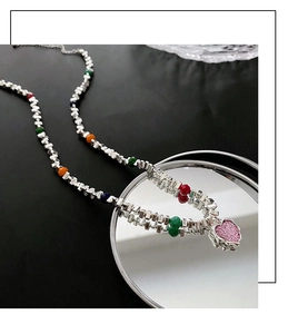 Gros plan d'un collier chaîne argentée avec perles colorées et pendentif cœur rose