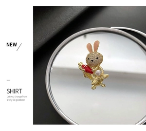 Close-up of cute rabbit brooch with white zircons, red carrot and pearl on mirror