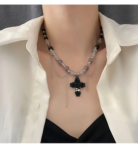 Détail du collier de perles avec pendentif croix rose et pompons métalliques