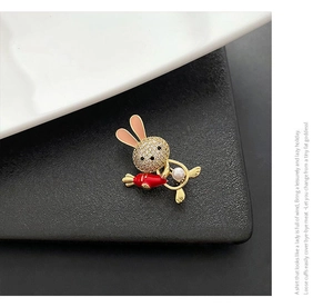 Close-up of golden bunny brooch with white zircon head, red carrot and pearl accent