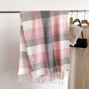 Dettaglio della sciarpa a quadri rosa e grigi con frange morbide appesa al muro bianco