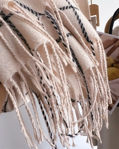 Detail of herringbone weave and fringe tassels on a beige plaid cashmere scarf