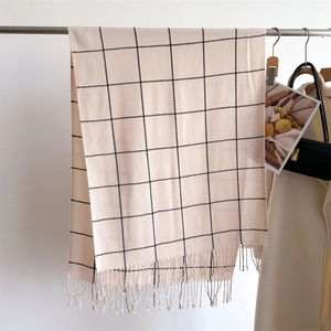 Detail of beige plaid cashmere scarf with fringes hanging on a minimalist hanger