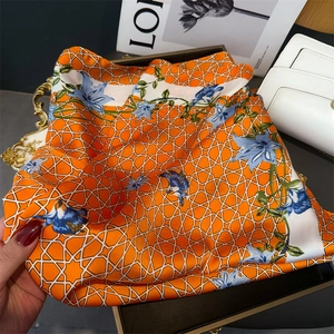 Detail of vibrant orange floral silk scarf displayed on a luxury gold tray with magazine
