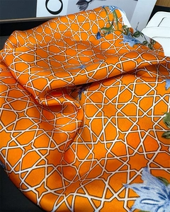 Detailed close-up of orange silk scarf with geometric patterns and floral motifs