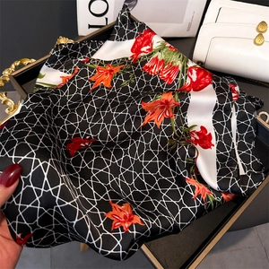 Detailed macro view of black floral silk scarf featuring orange flowers and geometric mesh