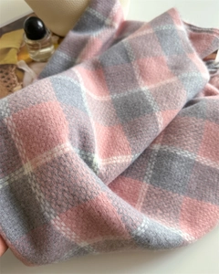 Gros plan d'une écharpe à carreaux rose et gris avec texture douce et franges