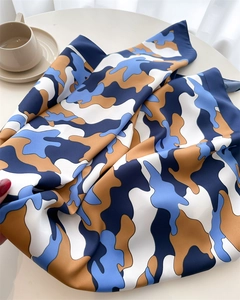 Detail showing the smooth silk texture and blue cloud pattern of the square scarf