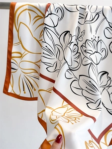 Detail of artistic lily print on white silk scarf with luxury orange border trim