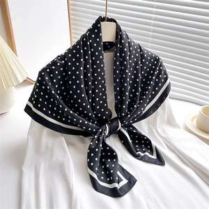 Elegant polka dot silk scarf styled on a white blouse against a minimalist home background