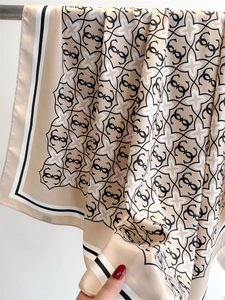Dettaglio di sciarpa in seta champagne con stampa di stelle e monogramma dal drappeggio morbido