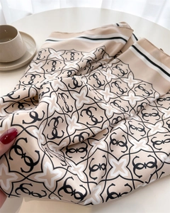 Dettaglio di un foulard in seta beige con motivo geometrico G e bordo a righe