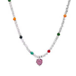 Collier chaîne argentée avec perles colorées et pendentif cœur rose sur fond blanc