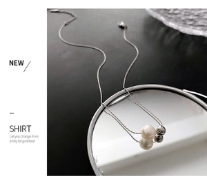 Détail d'un collier chaîne serpent avec une perle blanche et une bille en acier poli