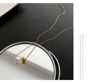 Détail macro du collier en titane doré avec perle ronde et perle en or poli sur miroir