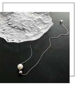Gros plan d'un collier minimaliste en titane argenté avec perle blanche et boule en métal