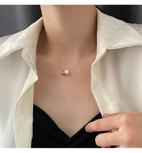 Détail d'un collier en acier titane doré avec une perle ronde et un pendentif doré