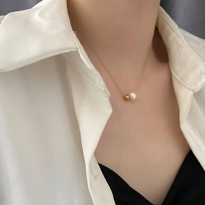 Collier minimaliste en acier titane avec perle dorée et perle blanche porté par mannequin