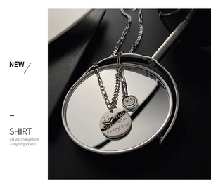 Macro detail of layered silver titanium steel necklace with smile face pendant and engraving
