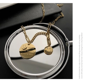 Detail of gold layered smile pendant necklace featuring engraved wish message on round disk