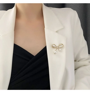 Detailed view of an elegant gold bow brooch with pearl drops on a white blazer