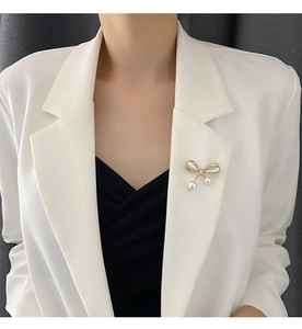 Close-up of golden bow brooch with white pearls on a white blazer lapel