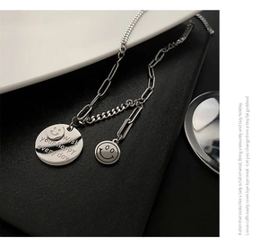 Detail of silver smiley face necklace with chunky mixed chains and engraved metal pendant