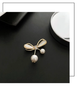 Macro shot of elegant gold bow brooch featuring white shell wings and dangling pearls