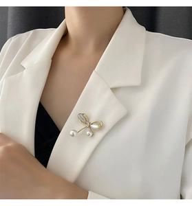 Detail view of a pearl bow brooch pinned on a white blazer lapel for an elegant look