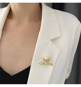 Detailed view of an elegant gold plant branch brooch with pearls on a white blazer lapel