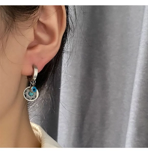 Close-up of silver hoop earrings with blue evil eye and sun charms on model