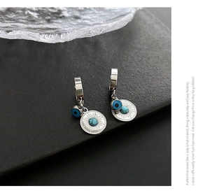 Detail of silver drop earrings featuring radial sunburst disk and blue evil eye charm