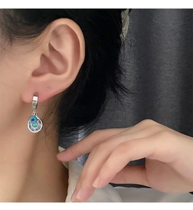 Detail of silver drop earrings with blue evil eye pendant on model against grey background