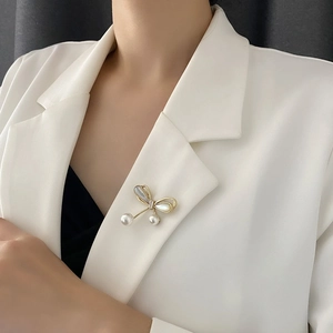 Elegant gold bow brooch with pearl drops and shell inlay on a white blazer lapel