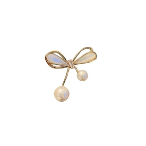 Elegant gold bow brooch with pearlescent inlay and two hanging white pearls on white background