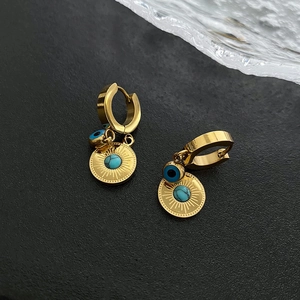 Golden Evil Eye hoop earrings with blue sunburst charms on a dark stone surface
