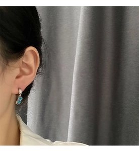 Détail de boucles d'oreilles œil de démon en acier titane avec perles bleues sur modèle