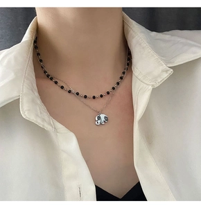 Detail of double-layer necklace with black beads and a silver elephant pendant on a model