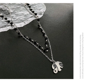 Detail of double-layer necklace with silver chain, black beads, and elephant pendant