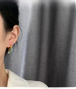 Dettaglio ravvicinato di orecchini a cerchio dorati con perle azzurre su modella