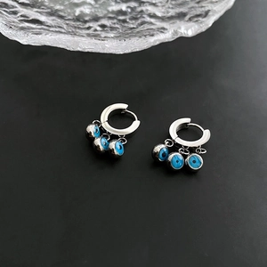 Boucles d'oreilles créoles œil bleu en argent avec perles sur fond sombre texturé