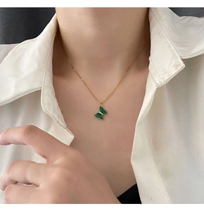 Dettaglio di una collana in titanio dorato con ciondolo a farfalla in cristallo verde
