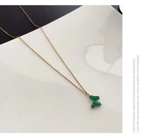 Dettaglio macro di una collana a farfalla dorata con ali in cristallo verde smeraldo