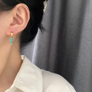 Orecchini a cerchio dorati con tre pietre turchesi indossati da modella in bianco