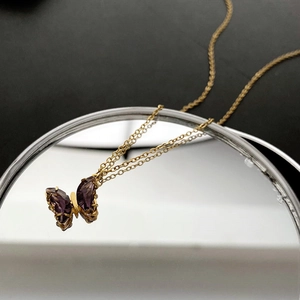 Collana in titanio dorato con pendente a farfalla in cristallo viola su superficie a specchio