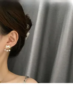 Detail of bow-shaped gold stud earrings with three hanging pearls on a female model